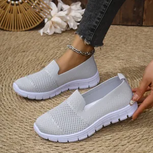 Detalle de zapatos slip-on de malla transpirable gris claro para mujer en alfombra.