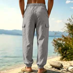 Back view of men's loose grey linen cargo pants with elastic cuffs on a sunny beach