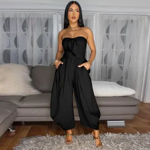 Elegant black strapless jumpsuit with front tie detail in a cozy home living room setting.