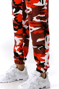 Close-up of men's red and orange camouflage joggers with elastic cuffs and white sneakers.