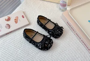 Close-up view of elegant black sequined girls flat shoes with bow and elastic strap detail