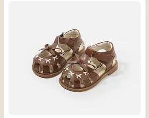 Detailed macro shot of brown toddler girl sandals featuring elegant white bow embroidery