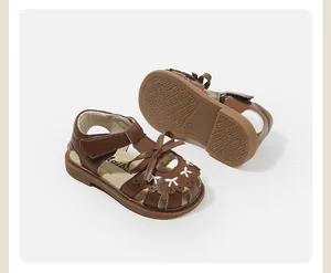 Close-up detail of brown toddler sandals featuring bow accents and flexible rubber soles.