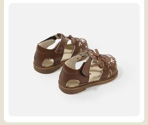 Classic brown baby girl sandals with charming bow and decorative white stitching detail.