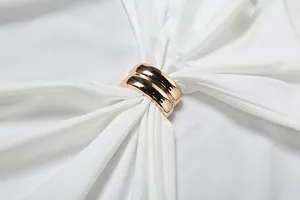Close-up detail of the decorative gold metal ring on a white sleeveless halter neck top