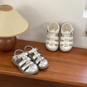 Detail of two pairs of toddler sandals in silver and white finishes on a wooden surface.