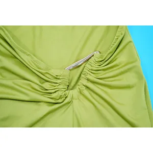 Macro detail view showing the gold metallic hardware and pleated fabric on green dress