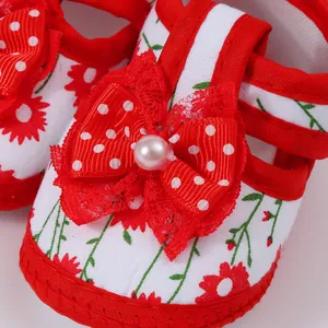 Detail shot of red polka dot bow with pearl on floral baby girl walking shoes