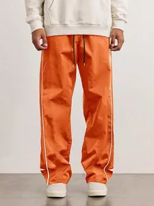 Close-up view of orange men's high street sports pants featuring white side stripe details