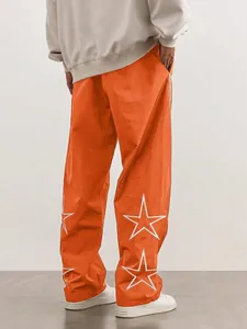 Detail view of men's high-street orange track pants featuring white star embroidery