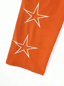 Close-up of white star embroidery on orange high street fashion jogger pants detail.