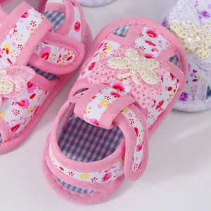 Close-up of pink floral baby sandals with butterfly bow and pearl accents.