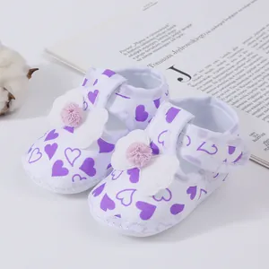 Close-up of baby girl sandals with purple heart patterns and decorative white bows.