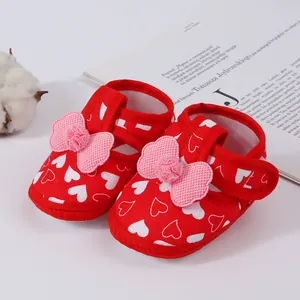 Close-up of red baby walking shoes with white heart pattern and pink decorative bows