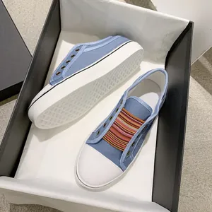 Detailed view of blue canvas sneakers featuring colorful striped elastic bands in a black shoebox
