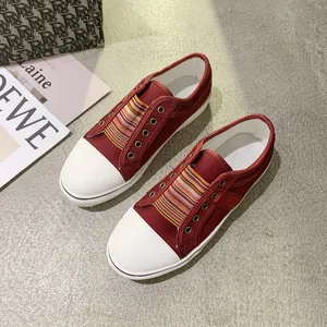 Detailed view of wine red canvas shoes with colorful striped tongue and white toe cap.