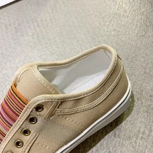 Close-up of khaki canvas shoe heel featuring colorful striped elastic band and metal eyelets