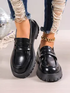 Close-up of stylish black platform chunky loafers with thick serrated sole on foot