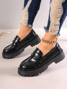 Close-up view of black platform loafers featuring chunky lug soles and gold chain anklet