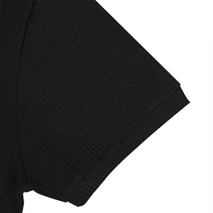 Detalle de la manga de un polo negro transpirable con textura de punto piqué acanalado.