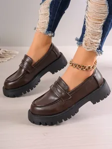 Close-up of brown platform loafers with chunky sole and stylish gold chain anklet detail