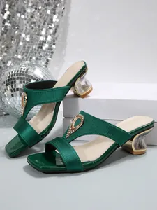 Detail view of emerald green satin mules with rhinestone accents and clear heels.