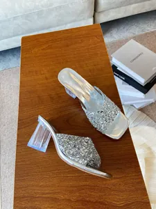 Primo piano di sandali glitter argento con tacchi a blocco trasparenti su tavolo in legno.