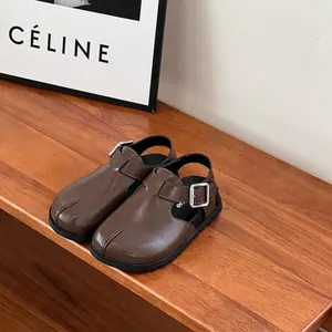 Detailed view of brown children's leather clogs with silver buckle on wooden bench