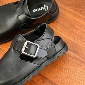 Close-up of black leather children's sandals with metal buckle and anti-slip sole.