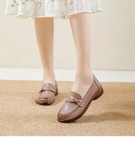 Elegant brown loafers with bow accent worn with white dress on a natural fiber mat