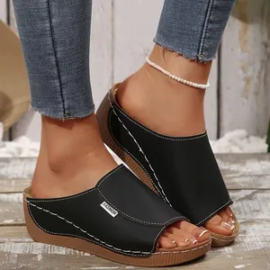 Close-up of black platform wedge sandals with white stitching details on wooden deck