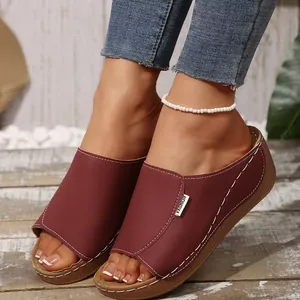 Close-up of burgundy platform wedge slides with white stitching on a model's foot.