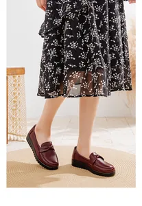 Gros plan de mocassins en cuir bordeaux portés avec une jupe fleurie sur un tapis