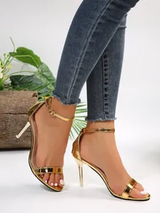 Elegant gold metallic stiletto sandals with ankle strap worn by a model in a studio setting.