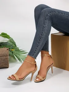 Detail of nude patent leather stiletto sandals with ankle strap and open toe design.