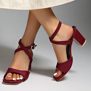 Elegante weinrote Sandalen mit Blockabsatz und Knöchelriemen an den Füßen des Models