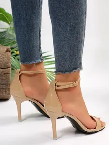 Close-up of nude patent leather stiletto sandals with an adjustable ankle strap design.