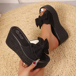 Primer plano de sandalias de cuña negras con un lazo elegante y diseño peep-toe.
