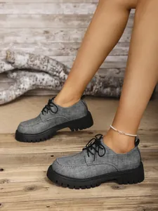 Nahaufnahme von grauen Oxford-Schuhen mit dicker schwarzer Plateausohle und Schnürung.