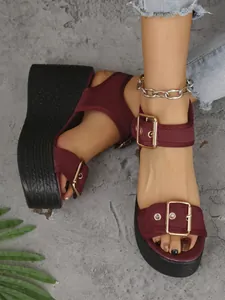Detailed view of burgundy wedge platform sandals with gold buckles on a model's feet