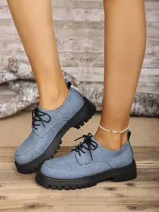 Nahaufnahme blauer Denim-Plateau-Loafers mit Knöchelschmuck auf Holzboden