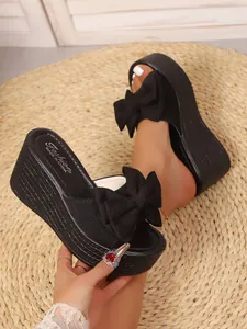 Primer plano de sandalias de cuña negras con un gran lazo decorativo