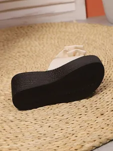 Vista detallada de sandalias de cuña negra con suela texturizada y lazo en color crema
