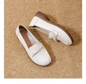 Detailed close-up of soft cream-colored loafers with twisted strap on a brown woven mat
