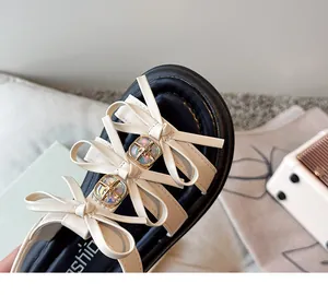 Close-up of girls' off-white sandals featuring delicate bow knots and iridescent crystals.