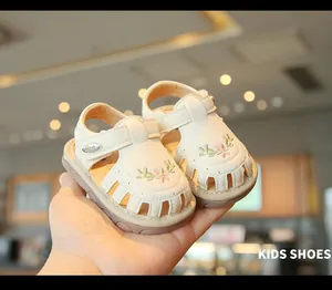 Nahaufnahme von beigen Baby-Sandalen mit Blumenstickerei und Lochmuster.