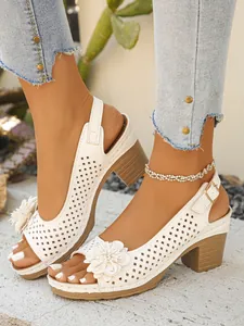 Macro view of white cutout block heel sandals featuring floral applique and buckle.