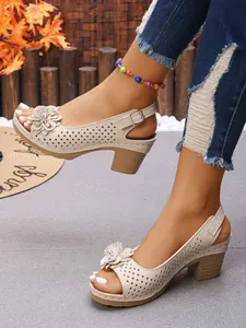 Detail view of beige chunky heel sandals with floral accents and hollow-out design