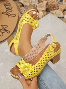 Close-up detail of stylish yellow hollow-out high-heel sandals with flower decoration.