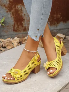 Close-up view of yellow hollow-out block heel sandals with flower detail on feet